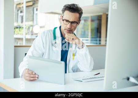 Male doctor using digital tablet while sitting at office Stock Photo