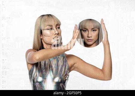 Female cyborg holding circular mirror with reflection of young woman over white background Stock Photo
