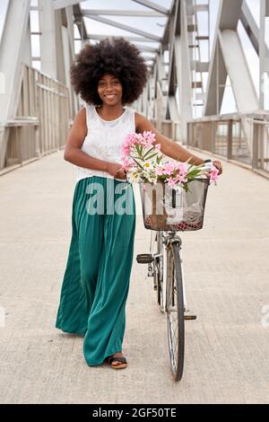 Afro woman walking with bicycle on bridge Stock Photo