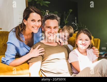 Man sitting with family near sofa at home during sunny day Stock Photo
