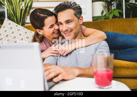 Smiling woman embracing man using digital tablet at home Stock Photo