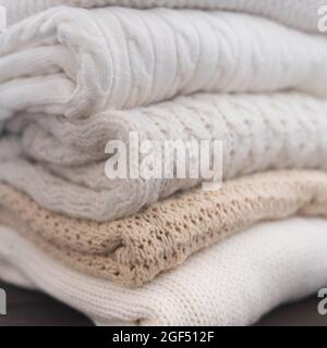 White and beige sweaters are stacked. Different knitted patterns. Autumn or winter background. Stock Photo