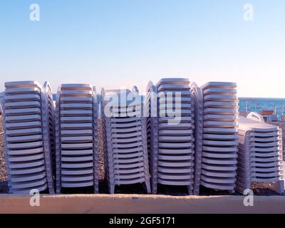 Beach white sun loungers stacked on top of each other stand in row on the seashore under the blue sky Stock Photo