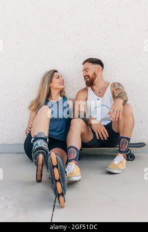 Happy young couple looking at each other while sitting in front of wall Stock Photo