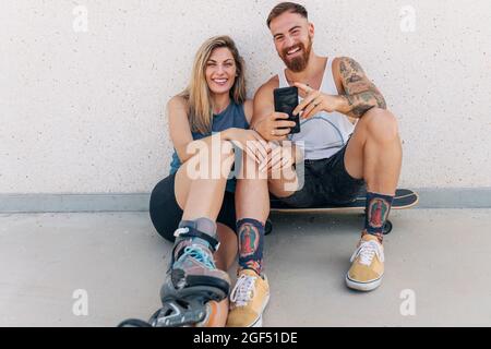 Happy young couple with smart phone leaning on wall Stock Photo