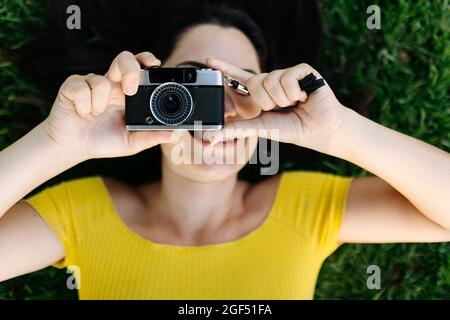 Young woman photographing through camera while lying on grass Stock Photo