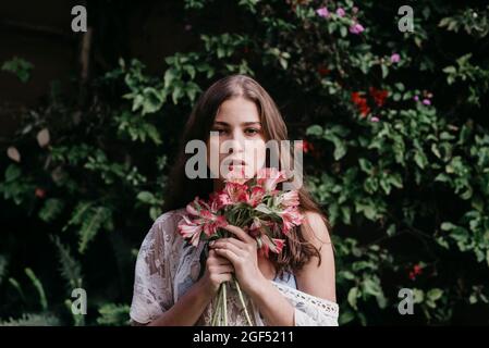 Beautiful young woman with flowers in front of ivy plants Stock Photo