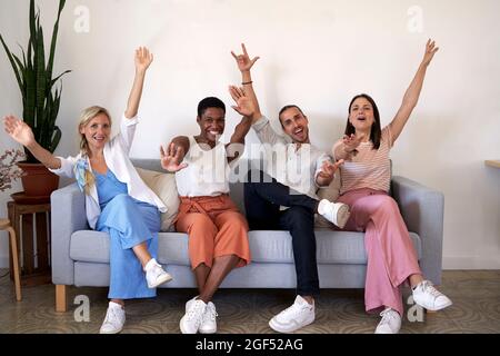 Male and female coworkers cheering while sitting on sofa Stock Photo