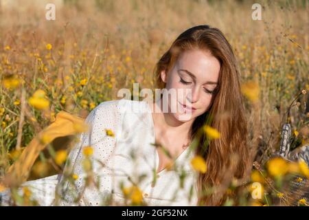 Young redhead woman with eyes closed sitting amidst flowers Stock Photo