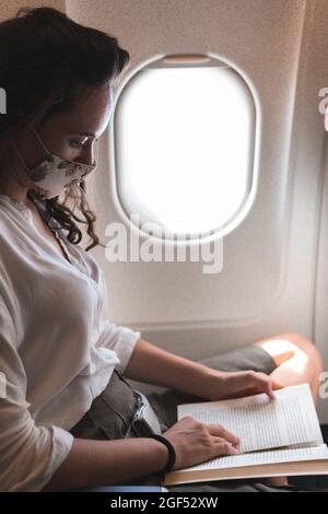 Businesswoman reading book while traveling in airplane during COVID-19 Stock Photo