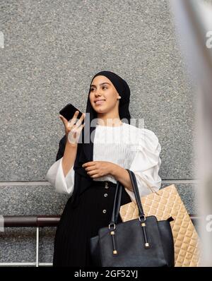 Woman sending voicemail through mobile phone in front of wall Stock Photo