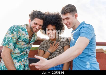 Young male and female friends laughing while looking at smart phone Stock Photo