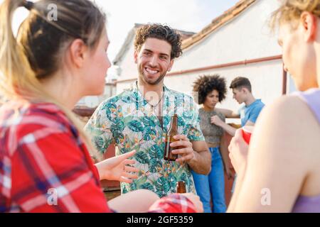 Young male and female friends having drinks on rooftop during party Stock Photo