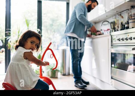 Girl sitting on rocking horse toy while father at kitchen counter Stock Photo