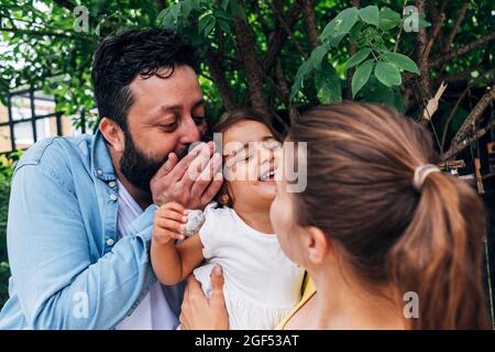 Father whispering in ear of daughter while playing with mother at back yard Stock Photo