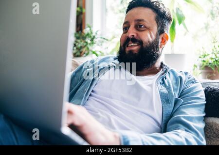 Smiling bearded man using laptop while working at home Stock Photo