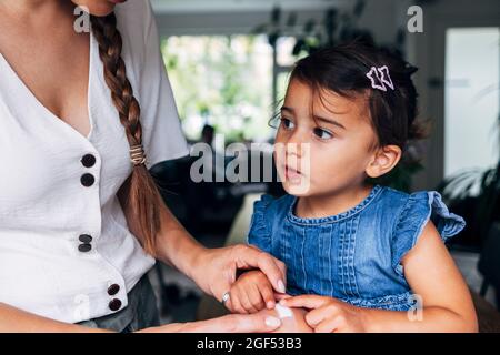 Woman putting adhesive bandage on girl's knee at home Stock Photo