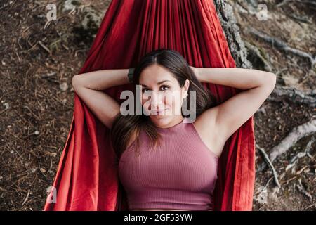 Beautiful young woman with hands behind head relaxing on hammock Stock Photo