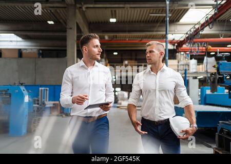 Male professionals discussing while walking in factory Stock Photo