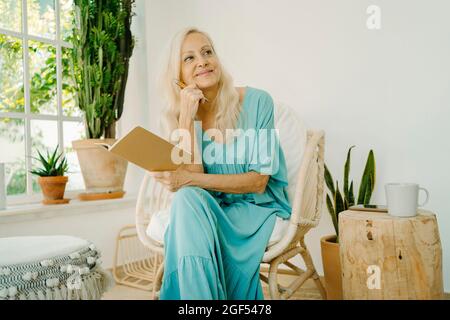 Thoughtful senior woman looking away holding book at home Stock Photo