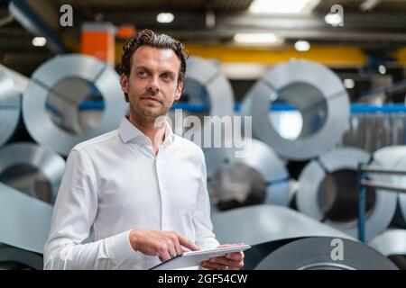 Thoughtful businessman holding digital tablet in factory Stock Photo