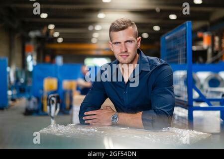 Confident young businessman staring while leaning on cardboard box Stock Photo