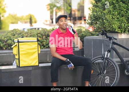Happy delivery man looking away while talking on smart phone Stock Photo