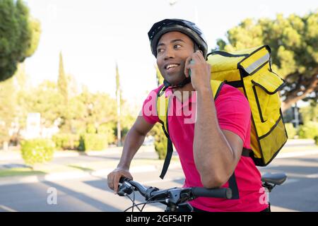 Smiling delivery man talking on smart phone while leaning on bicycle Stock Photo