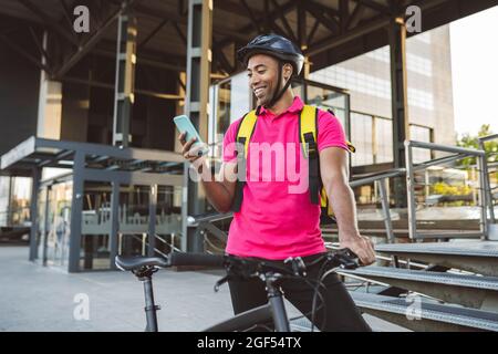 Smiling delivery man text messaging through smart phone while standing with bicycle Stock Photo
