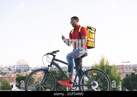 Delivery man wearing sunglasses text messaging through smart phone while standing with bicycle Stock Photo
