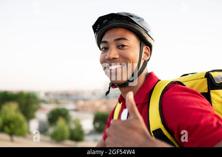 Smiling delivery man wearing helmet gesturing thumbs up Stock Photo