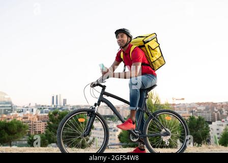 Male delivery person holding smart phone looking away while leaning on bicycle Stock Photo