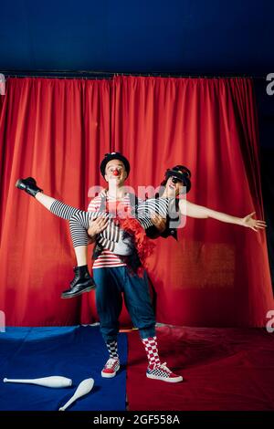 Male clown carrying female performer while performing on circus stage Stock Photo