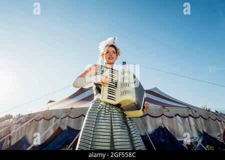 Female performer playing accordion in front of circus tent Stock Photo