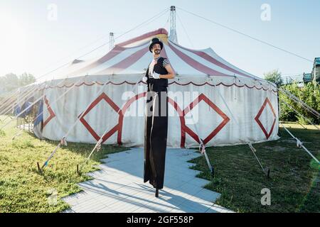 Male artist in costume standing on stilts in front of circus tent Stock Photo