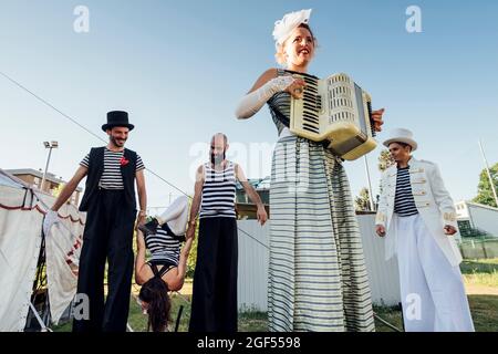 Female artist playing accordion while performers in background at circus Stock Photo