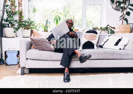 Senior businessman examining laptop while sitting on sofa at home Stock Photo