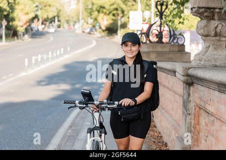 Smiling young female delivery person wheeling bicycle Stock Photo