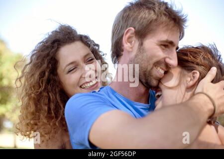 Happy curly haired woman looking at young couple embracing in park Stock Photo