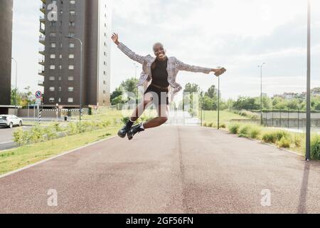 Happy young woman clicking heels while jumping on road during sunny day Stock Photo