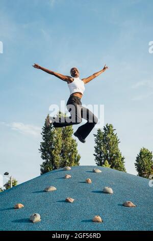 Happy woman with arms outstretched jumping on climbing wall at park Stock Photo
