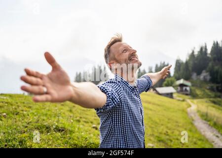 Happy man standing with arms outstretched on mountain Stock Photo
