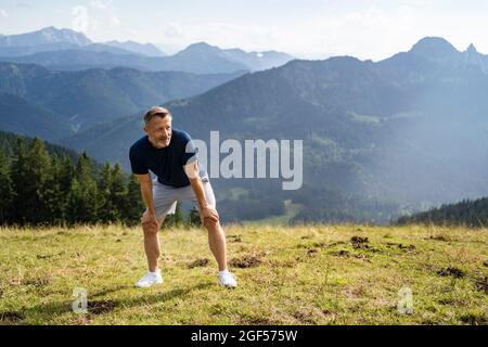 Tired man with hands on knees at mountain during sunny day Stock Photo