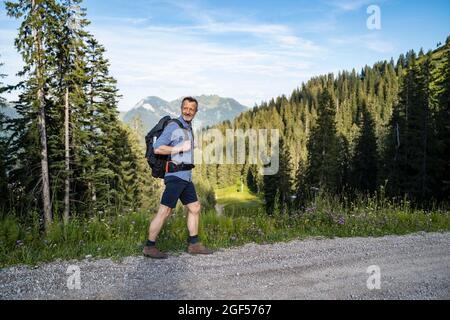 Male hiker with backpack looking over shoulder while walking on dirt road Stock Photo