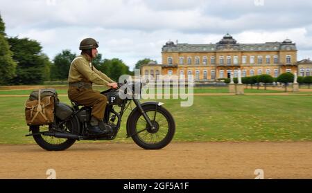 World War 2 despatch rider in uniform on classic  motorcycle riding past stateley home. Stock Photo