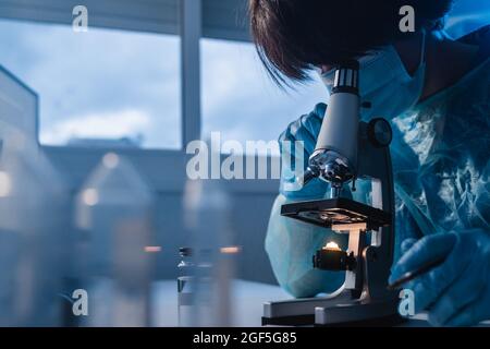 Asian medical scientist using microscope analyzing covid samples inside laboratory hospital - Focus on lens Stock Photo