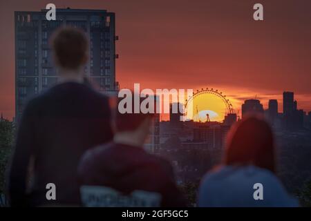 London, UK. 23rd August, 2021. UK Weather: Dramatic evening sun sets behind The London Eye ferris wheel viewed from top of Greenwich Park. Credit: Guy Corbishley/Alamy Live News Stock Photo