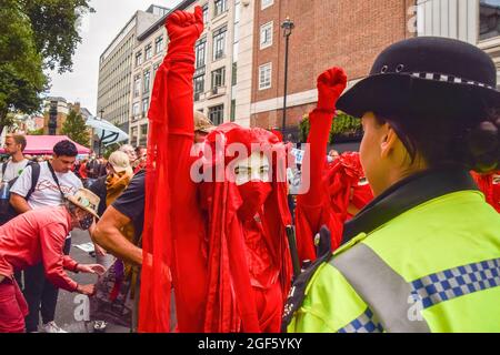 London, UK. 23rd Aug, 2021. Red Rebel Brigade demonstrators raise their fists in front of police officers during the protest in Covent Garden. Extinction Rebellion protesters gathered in central London for the start of their two-week campaign entitled Impossible Rebellion, calling on the UK Government to act meaningfully on the ecological and climate crisis. Credit: SOPA Images Limited/Alamy Live News