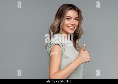 Young vaccinated woman with plaster on shoulder after getting covid-19 vaccine happy show thumb up Stock Photo