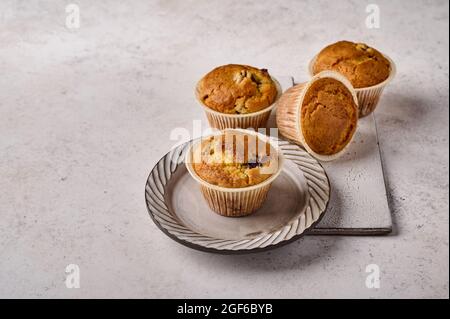 Homemade cupcakes in baking paper forms on plate and scratched ceramic cutting board on gray background, copy space Stock Photo